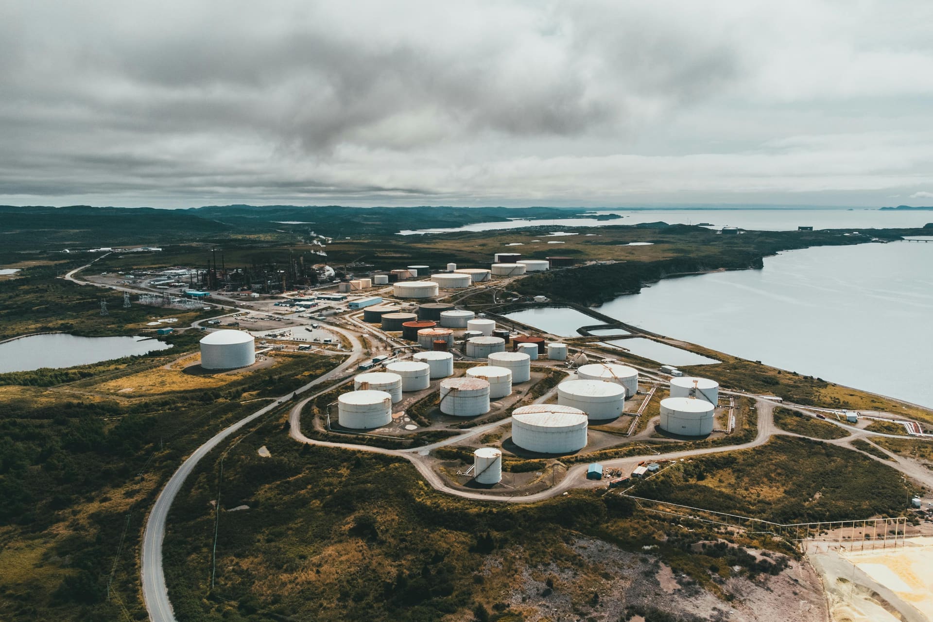 Aerial drone view of a coastal petroleum tank farm with road network leading toward the water.