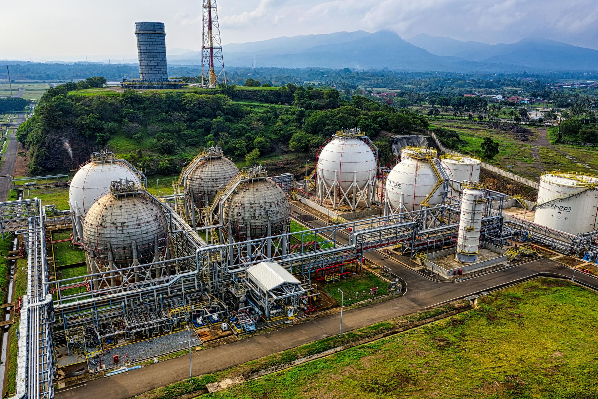 Aerial view of an LPG storage facility with white pressurized sphere tanks set against mountains.