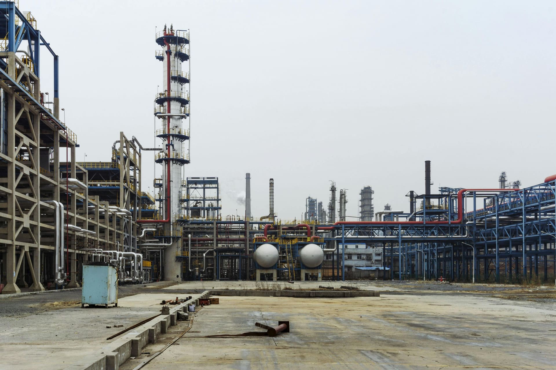 Ground-level view of an oil refinery and terminal complex with distillation towers, pipework and storage drums.